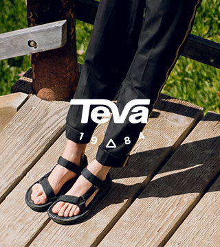 Person's feet standing on wooden stairs wearing Teva sandals.